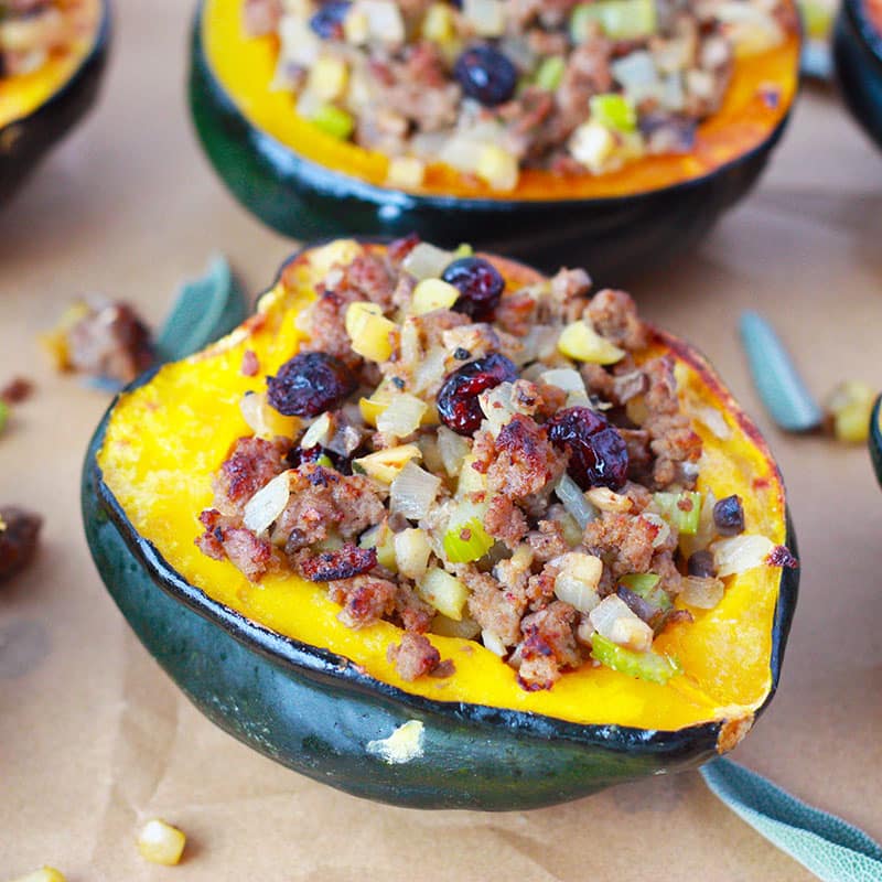 stuffed acorn squash with sausage, cranberries, celery, apples on a baking sheet