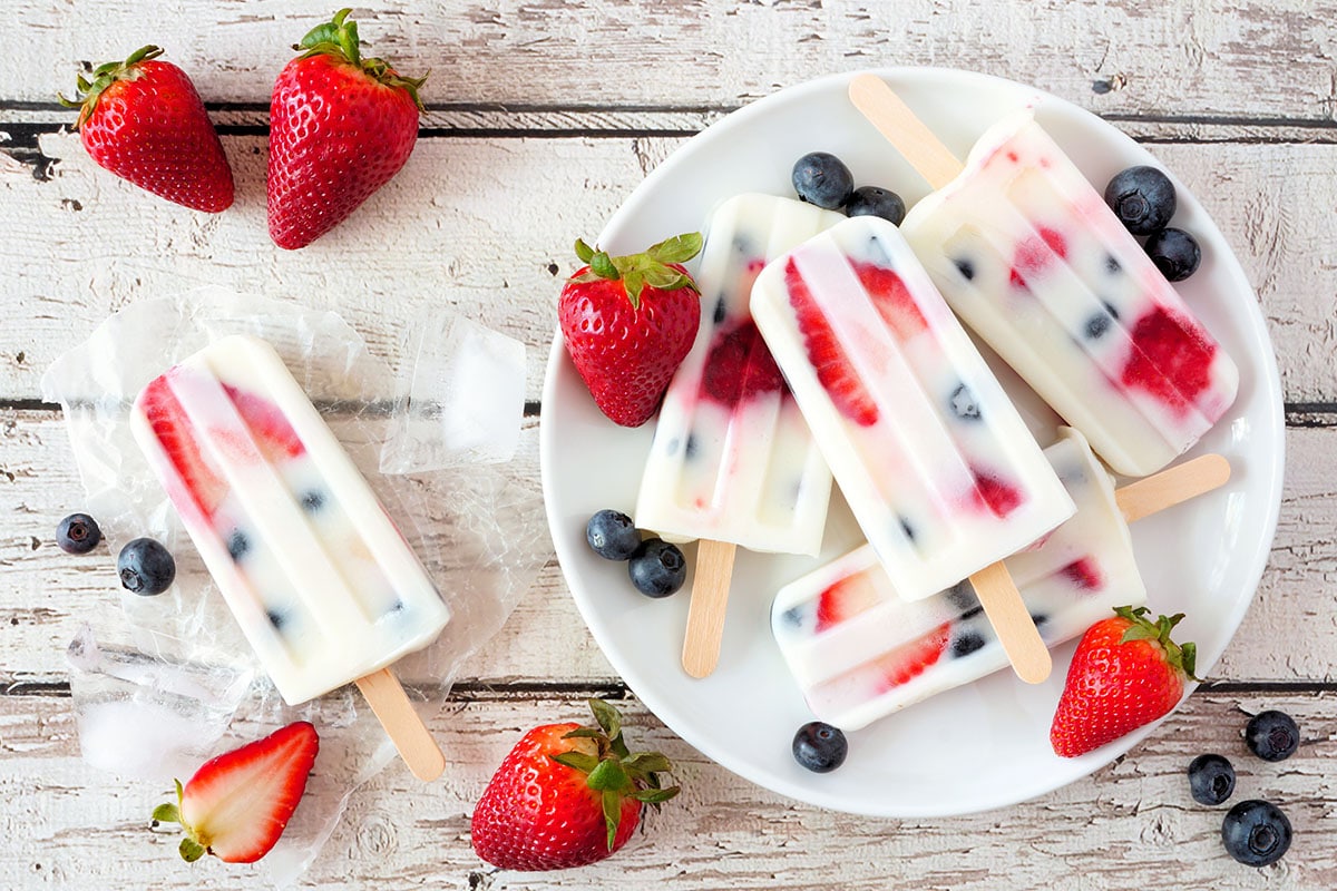 Healthy strawberry blueberry yogurt popsicles on a plate on a white wooden background view summer table scene
