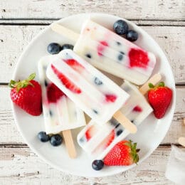 Healthy strawberry blueberry yogurt popsicles on a plate, top view summer table scene against a white wooden background