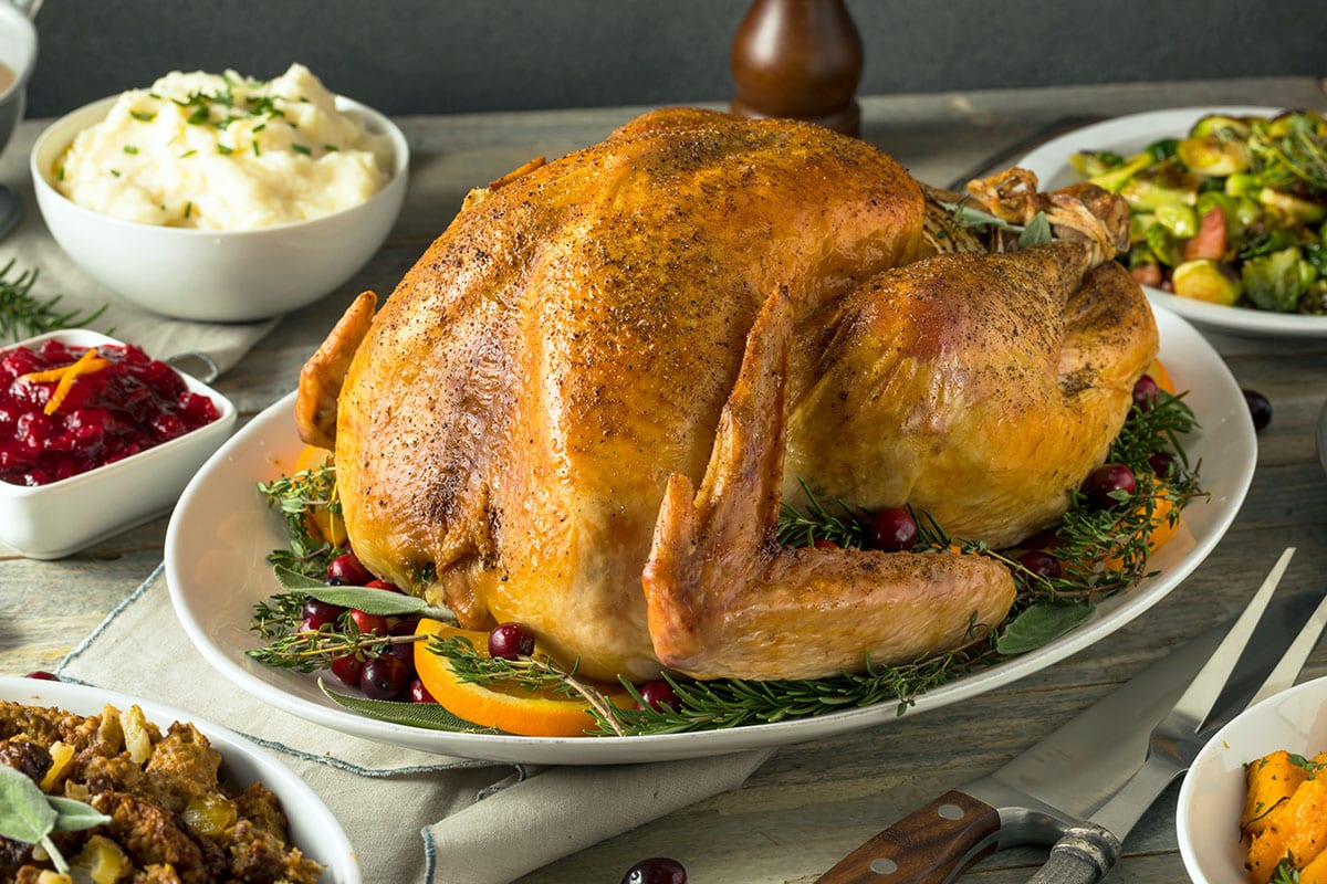 oven roasted turkey on a white platter for thanksgiving with sides on a table