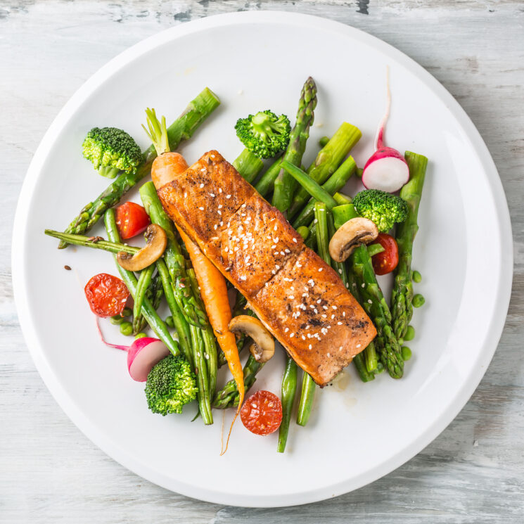 Bistecca di salmone arrosto con asparagi broccoli carote pomodori ravanelli fagiolini e piselli. Pasto di pesce con verdure fresche.