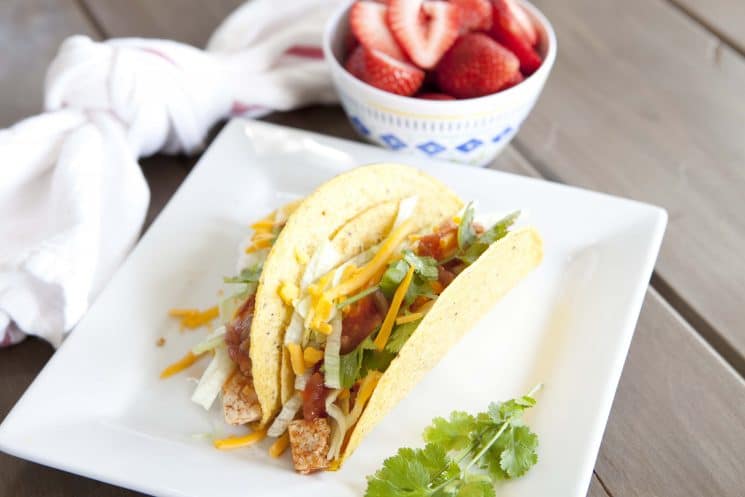 crunchy chicken tacos on a square plate served with strawberries