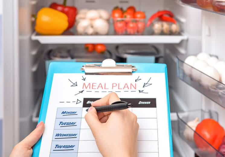 meal plan calendar on a meal plan and a person filling it out in front of an open fridge