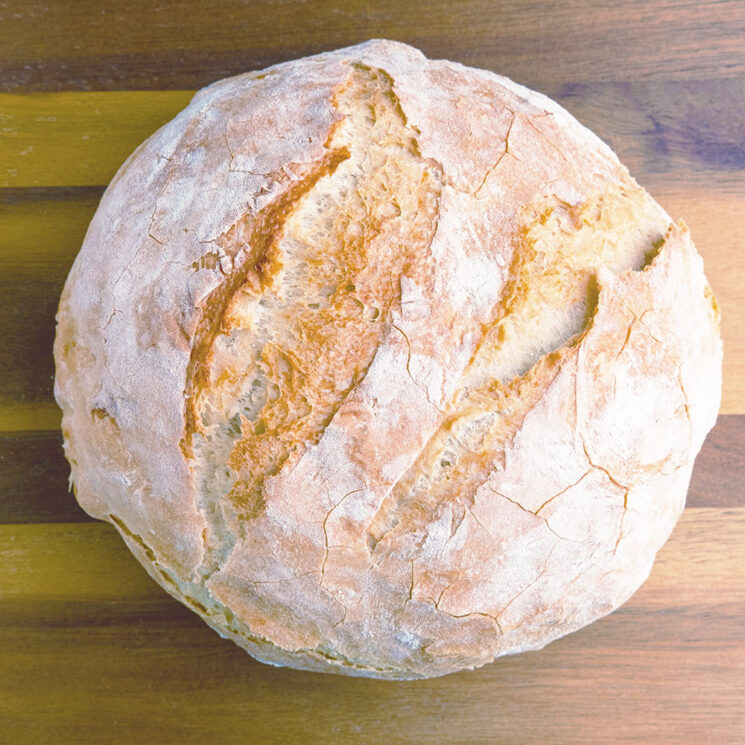 Artisan white bread baked in a cast iron dutch oven, one a cutting board waiting to be sliced