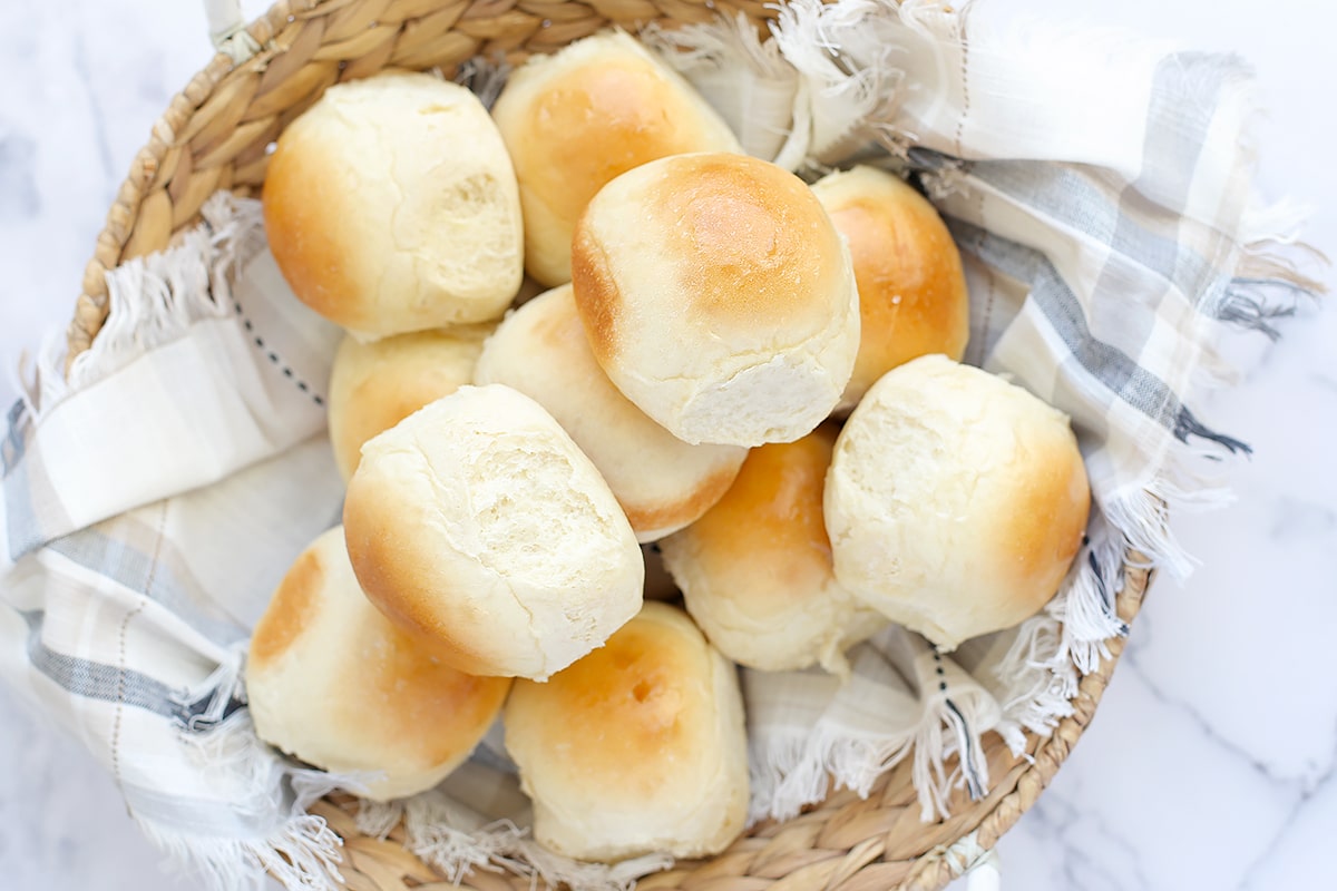 A basket of homemade dinner rolls in with a blue checkered linen.