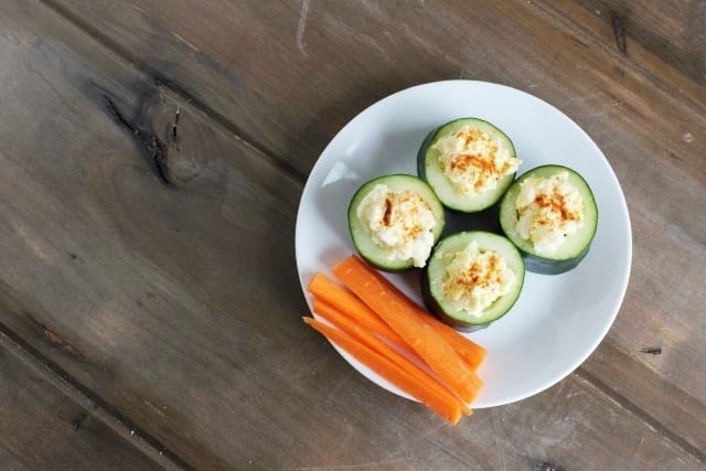 Loaded cucumber cups filled with egg salad and carrot sticks on the side.