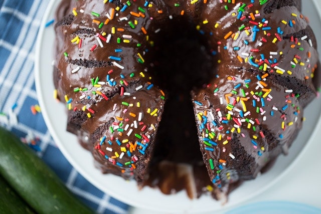 chocolate bundt cake topped with colorful sprinkles on a white cake plate