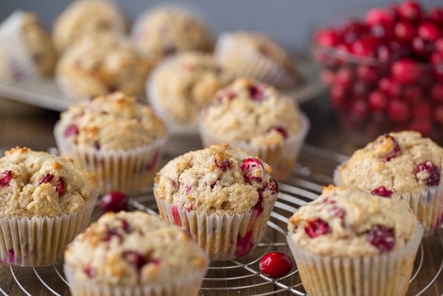 Cranberry muffins on a cooling rack with a bowl of cranberries in the background