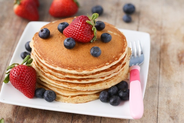 Close up of cottage cheese protein pancakes stacked on a plate with strawberries and blueberries