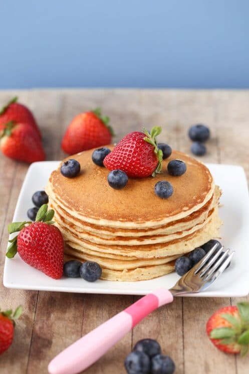 cottage cheese protein pancakes stacked on a plate with strawberries and blueberries and a pink fork