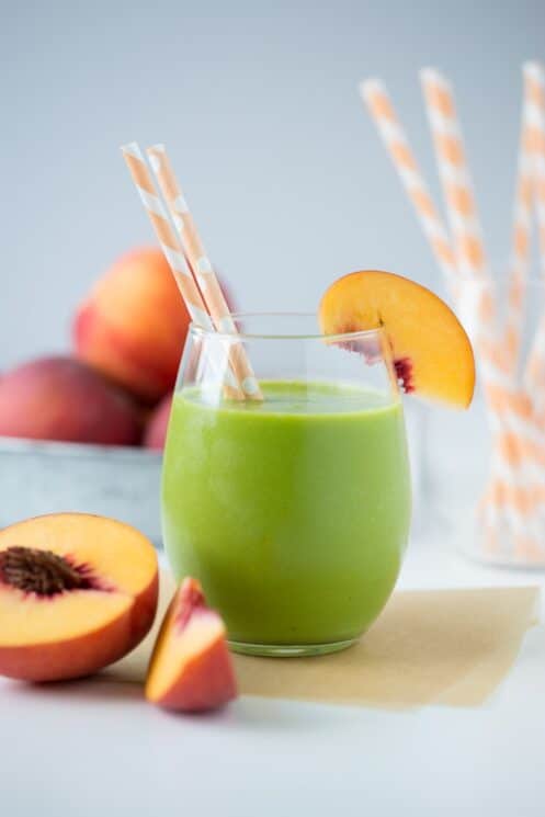 peachy green smoothie in a glass with straws