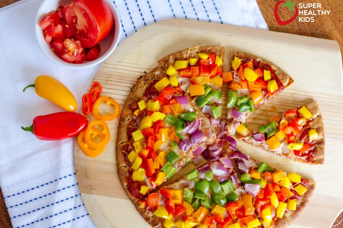 homemade pizza with rainbow colored bell peppers on a wooden board