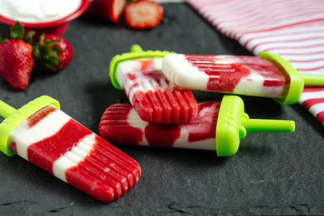 Strawberry creams on a dark background with green popsicle sticks