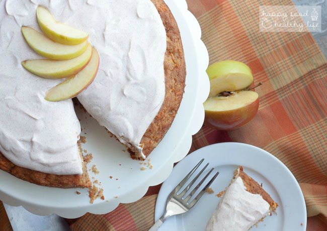 apple cake topped with white frosting  and sliced apples on a checkered tablecloth