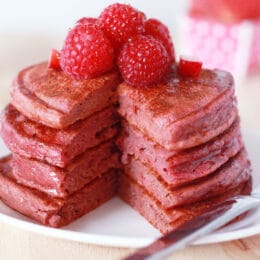 Stack of dye free pink pancakes on a plate with a slice taken out