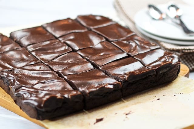 a sheet of brownies topped with chocolate frosting on a wooden cutting board