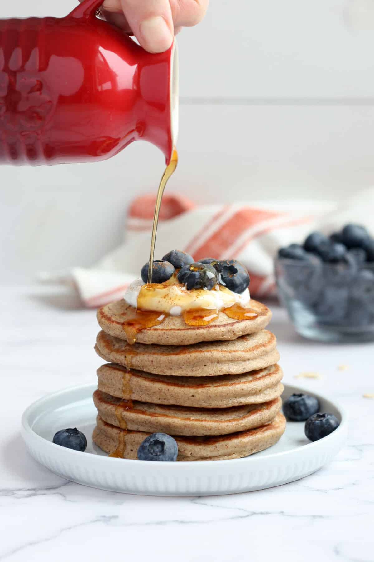 a stack of pancakes topped with blueberries being drizzled with maple syrup