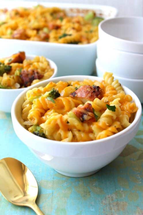 Pasta with cheese, chicken and broccoli in a white serving bowl with a stack of bowls in the background