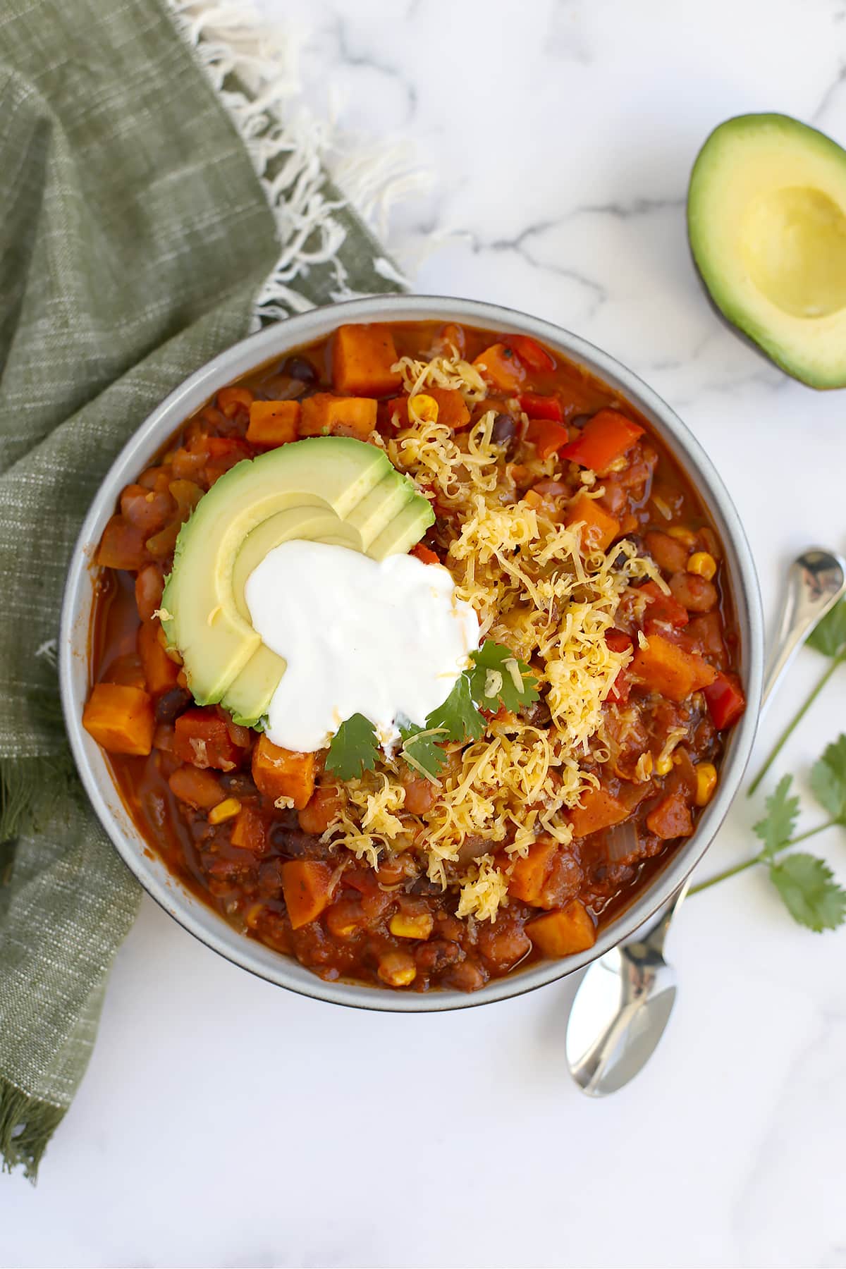 An overhead shot of vegetarian chili with sweet potatoes and black beans with a silver spoon and a green linen in the background.