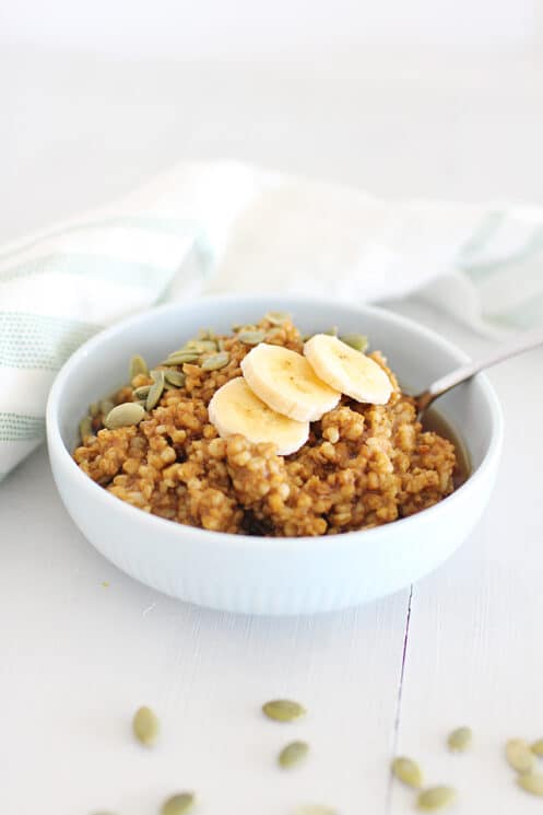 oatmeal topped with banana slices and pumpkin seeds served in a white bowl with a striped dish towel in the background