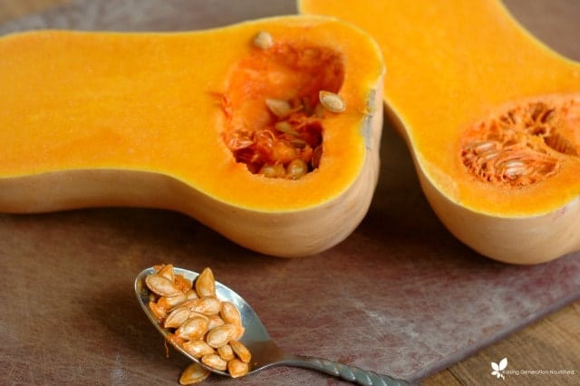 whole butternut squash cut in half with spoon scooping out seeds