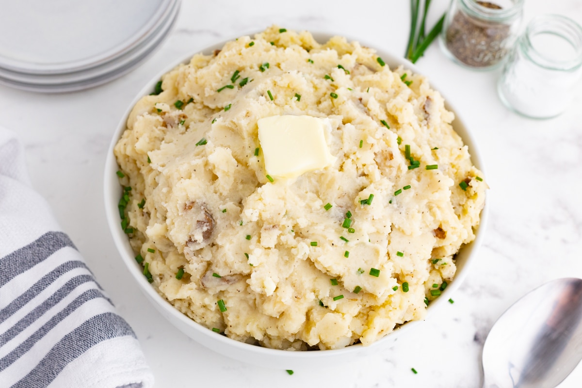 crockpot mashed potatoes in a white bowl with chives and butter on top, blue and white napkin in the background