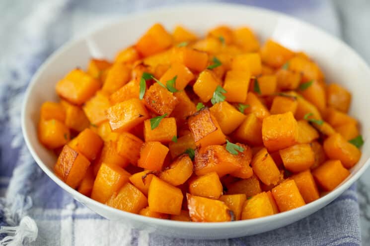 white bowl of beautifully caramelized butternut squash cubes with a sprinkle of parsley