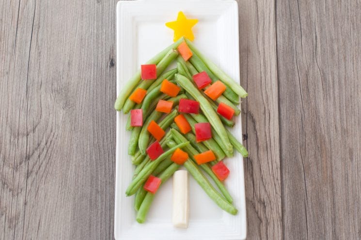 green beans and pepper pieces shaped into a christmas tree on a white plate
