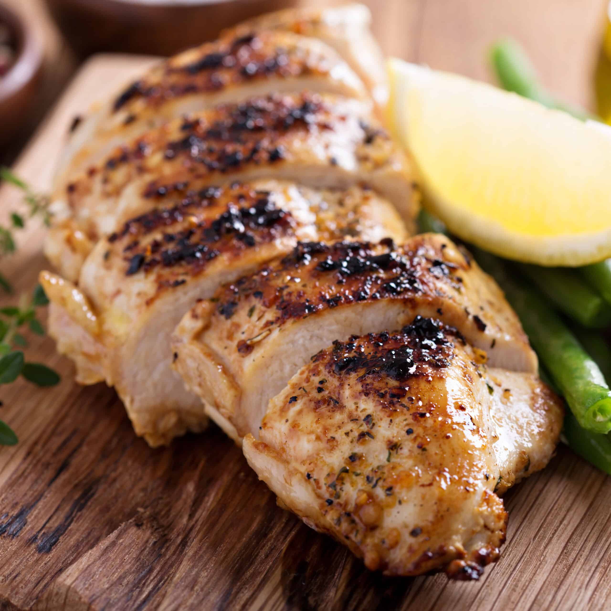 Grilled lemon chicken on a cutting board with thyme and green beans