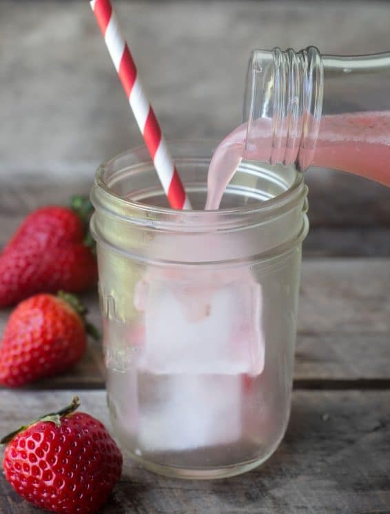 homemade soda being poured into a mason jar with a straw and fruit in the background
