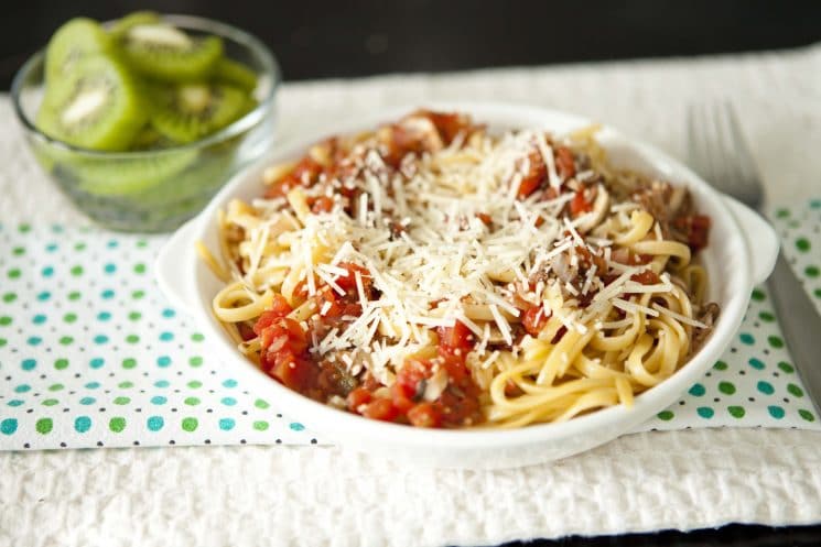 noodles with sauce and cheese with a decorative napkin served with kiwi