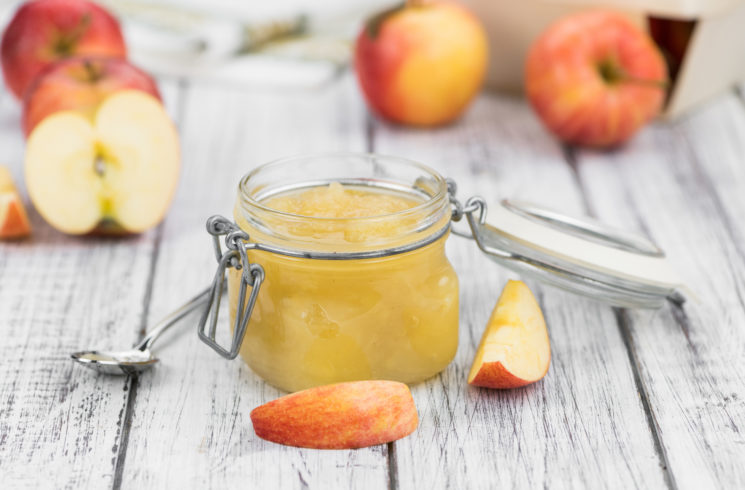 homemade applesauce in a glass jar with a hinged lid.  Apples in the background. 