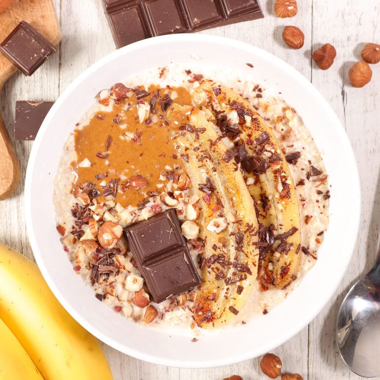 peanut butter banana oatmeal with banana slices, crushed nuts, and shaved chocolate