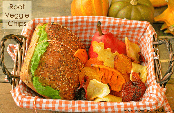 a basket surrounded by squash filled with root veggie chips and a sandwich