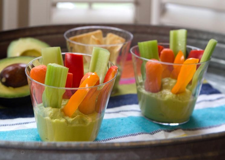 clear cups filled with green hummus and vegetable sticks on a metal tray