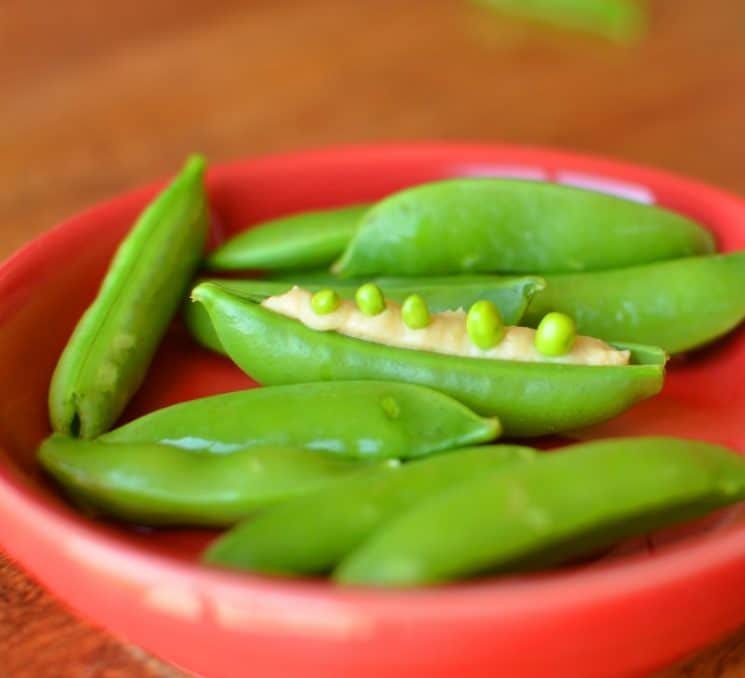 pea pods filled with hummus in a red bowl
