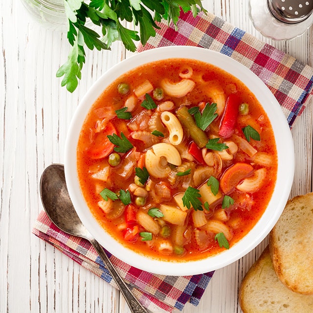 crockpot minestrone soup in a white bowl with crusty bread on the side