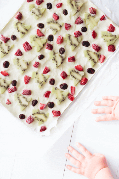 Tray of frozen yogurt topped with kiwi, strawberries and dried cranberries.