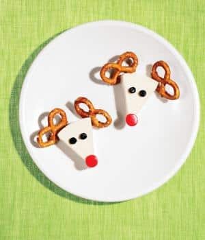 white triangle cheese with pretzel antlers on a white plate with a green background