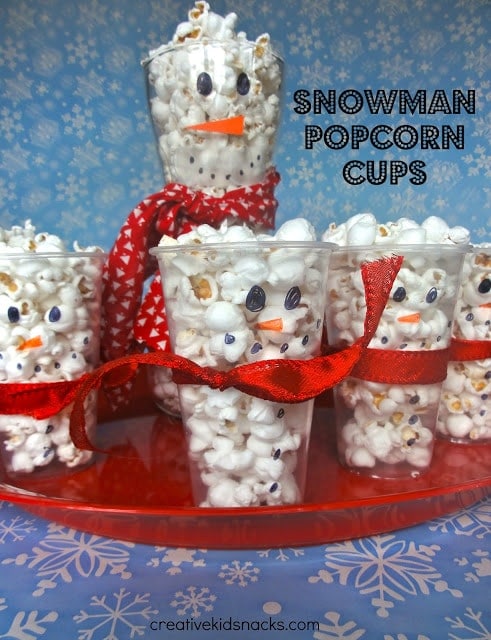 clear cups with a snowman face drawn on it filled with popcorn and tied with a ribbon