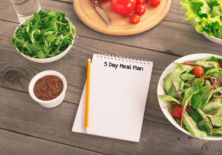 Blank notebook with various salad leaves, glass of water, tomatos and flax seed. Helpful balanced diet, weight loss and diet concept, top view