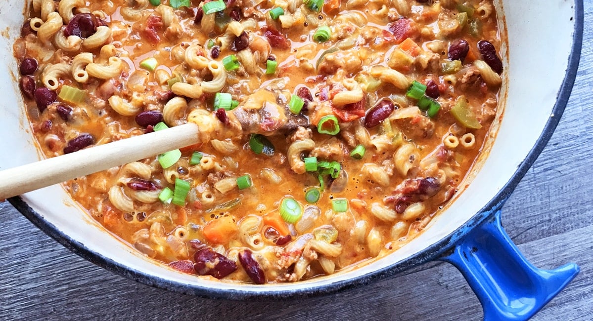 chili mac and cheese in a cast iron pot with a wooden spoon