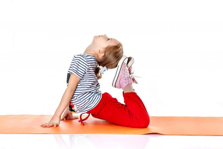 little girl doing yoga exercises on an orange yoga mat