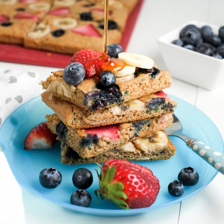 Pancake squares with berries and bananas on a blue plate drizzled with syrup