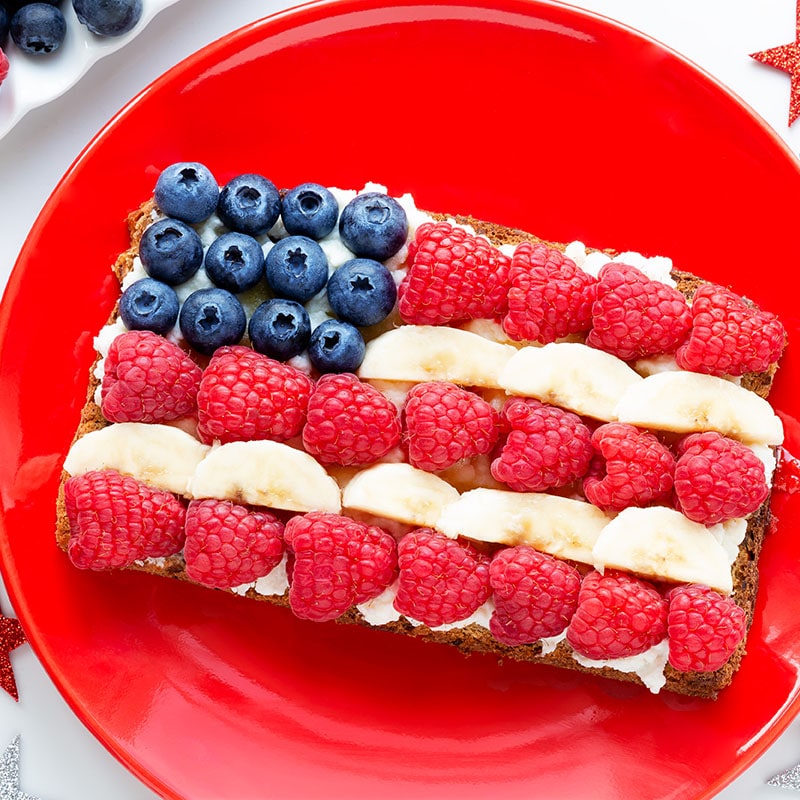 American flag ricotta toast with fresh fruit like raspberries, banana and blueberries on toast with patriotic decoration for Independence Day celebration