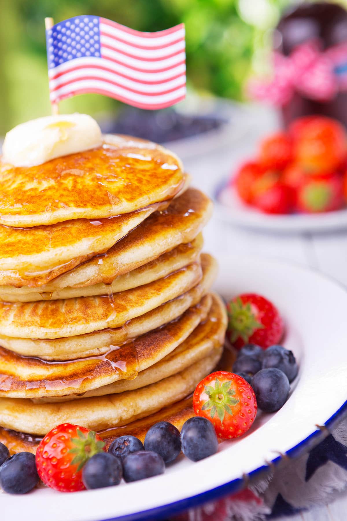 A stack of homemade whole grain pancakes with fresh berries, butter and syrup and an american flag on top