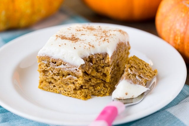 pumpkin cake with a creamy frosting on a white plate with pumpkins in the background