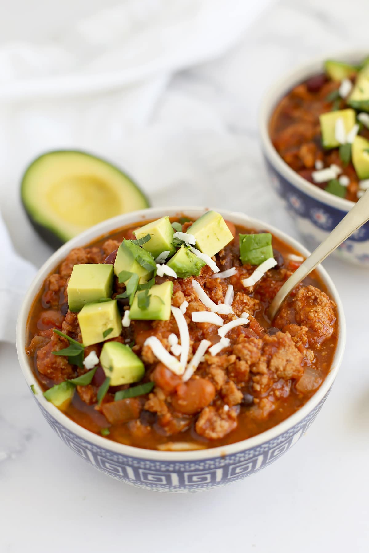 A close up image of ،memade chili topped with avocado and cheese with a gold s،.