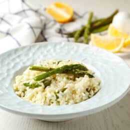 Delicious risotto with asparagus on white wooden table