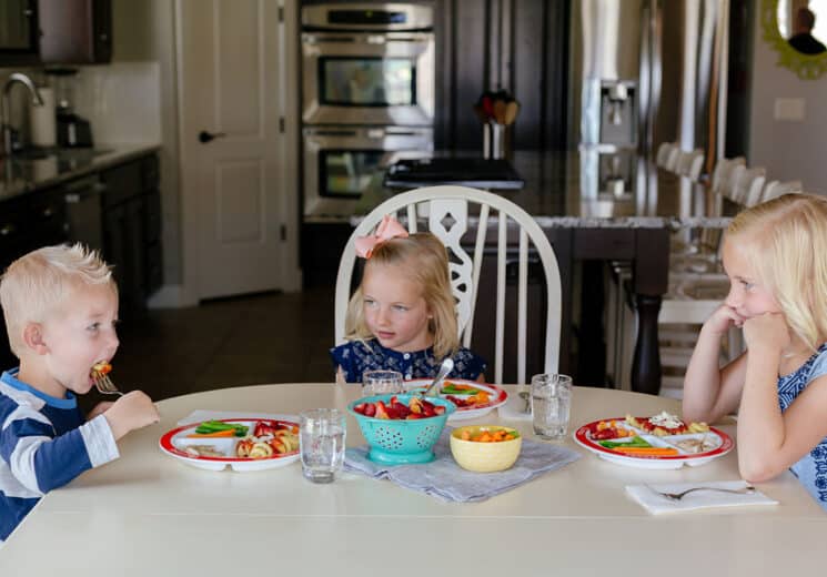 3 kinder sitzen an einem Esstisch essen und lernen Tischmanieren